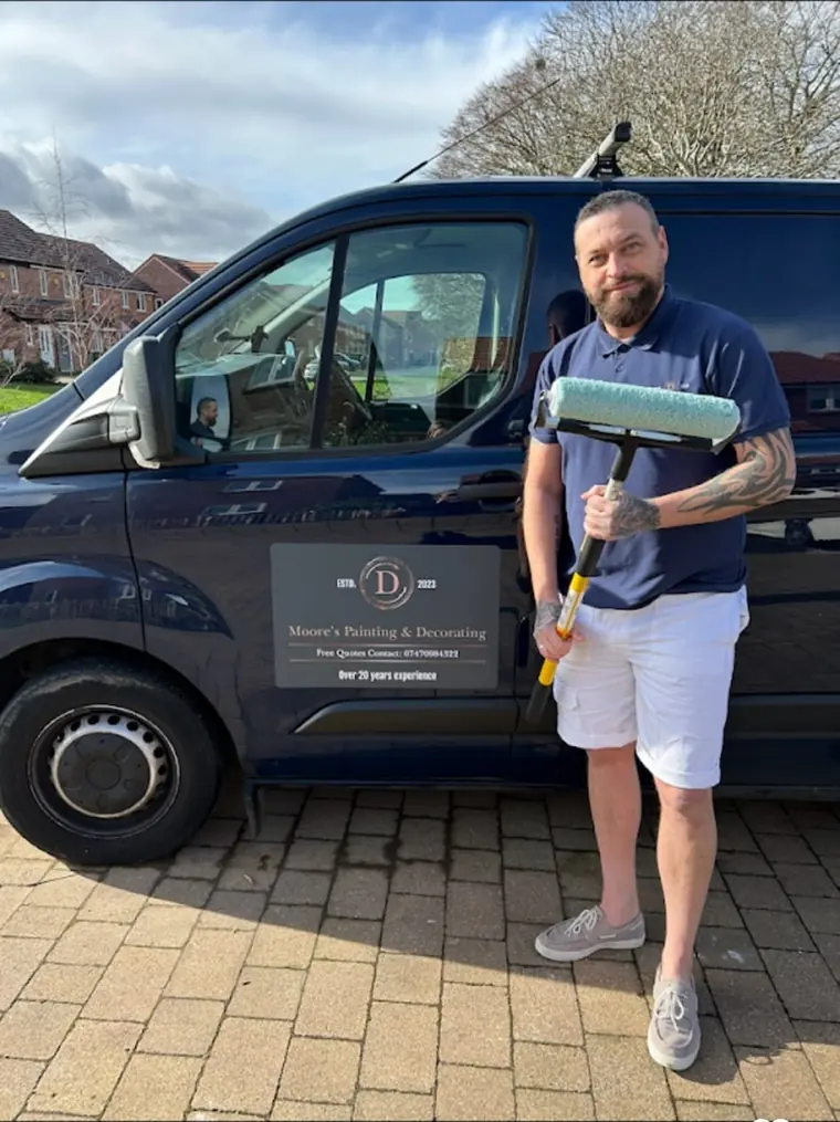Darren Moore standing beside the Moore's Painting and Decorating van in Andover, holding a paint roller