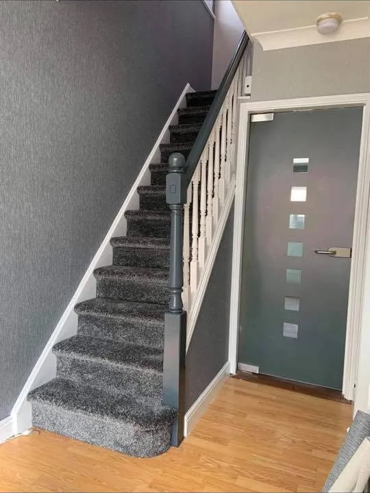 The same staircase after decorating, with fresh paintwork, a new grey runner and a painted front door