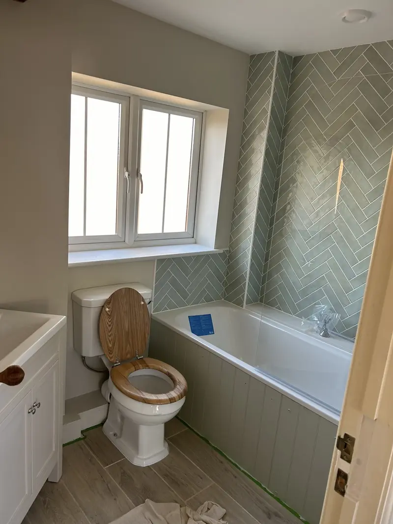 Family bathroom repainted in soft white beside a green herringbone tiled bath recess