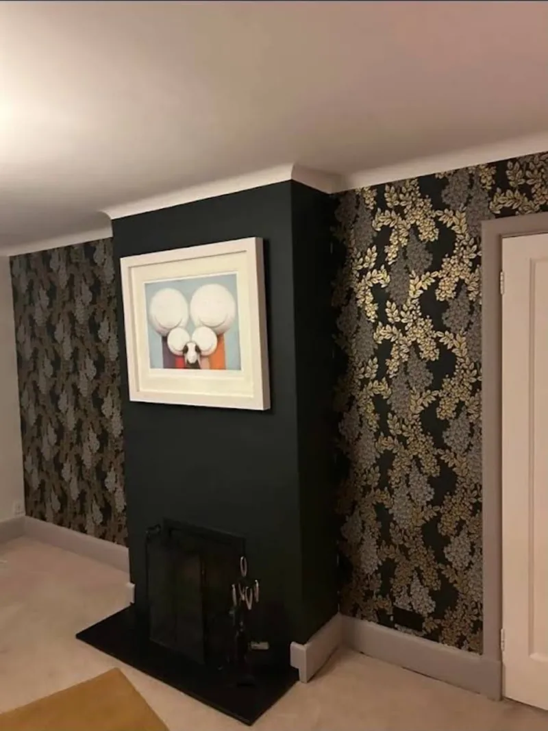 Chimney breast painted deep green with gold and silver floral wallpaper either side in a Hampshire living room