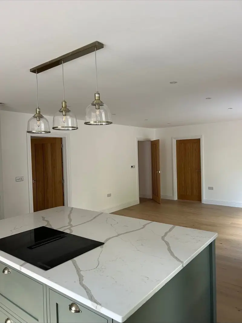 Kitchen island and units painted in a soft sage green under pendant lighting