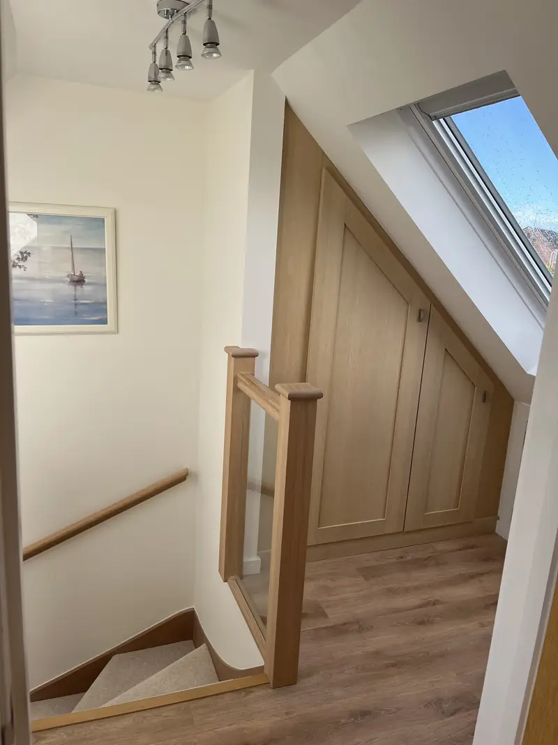 Loft landing finished in soft white with an oak balustrade and handrail beneath a velux